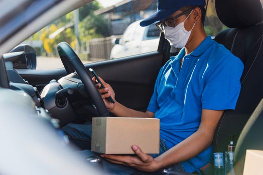 Asian delivery man courier online holding deliveries out boxes in car and using mobile phone contact the customer he protective face mask service under curfew quarantine pandemic coronavirus COVID-19