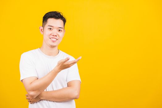 Portrait happy Asian handsome young man smiling standing wearing white t-shirt show something on hand he looking to camera, studio shot isolated yellow background