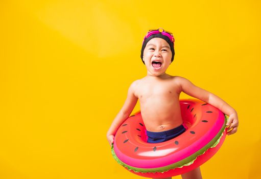 Summer vacation concept, Portrait Asian happy cute little child boy wear goggles and swimsuit hold watermelon inflatable ring, Kid having fun on summer vacation, studio shot isolated yellow background