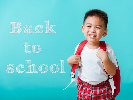 Back to school concept. Portrait closeup happy Asian cute little child boy in uniform smiling, isolated blue background. The kid from preschool kindergarten with a school bag backpack