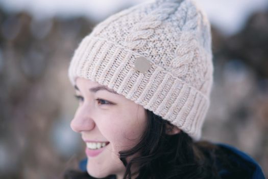 the beautiful young girl in a warm cap from wool of the alpaca in the winter forest. knitting