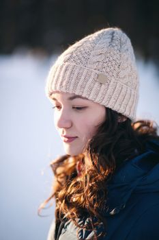 the beautiful young girl in a warm cap from wool of the alpaca in the winter forest. knitting