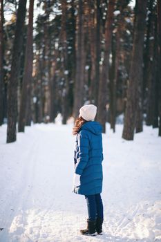 the beautiful young girl in a warm cap from wool of the alpaca in the winter forest. knitting