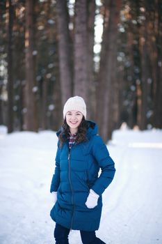 the beautiful young girl in a warm cap from wool of the alpaca in the winter forest. knitting