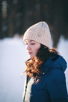 the beautiful young girl in a warm cap from wool of the alpaca in the winter forest. knitting