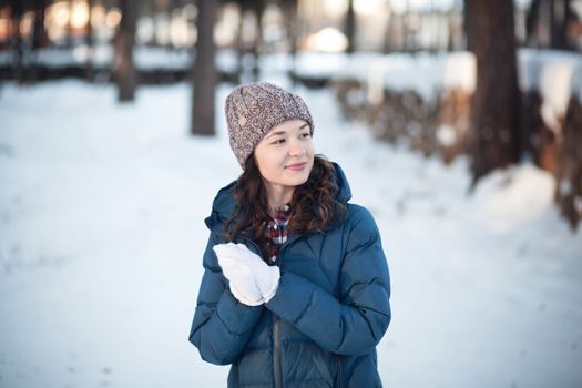 the beautiful young girl in a warm cap from wool of the alpaca in the winter forest. knitting