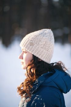 the beautiful young girl in a warm cap from wool of the alpaca in the winter forest. knitting