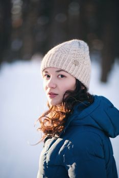the beautiful young girl in a warm cap from wool of the alpaca in the winter forest. knitting