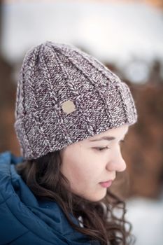 the beautiful young girl in a warm cap from wool of the alpaca in the winter forest. knitting