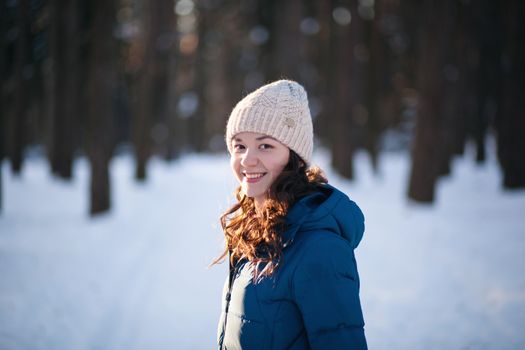 the beautiful young girl in a warm cap from wool of the alpaca in the winter forest. knitting