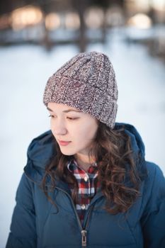 the beautiful young girl in a warm cap from wool of the alpaca in the winter forest. knitting