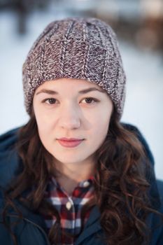 the beautiful young girl in a warm cap from wool of the alpaca in the winter forest. knitting