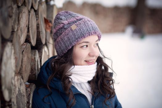 the beautiful young girl in a warm cap from wool of the alpaca in the winter forest. knitting