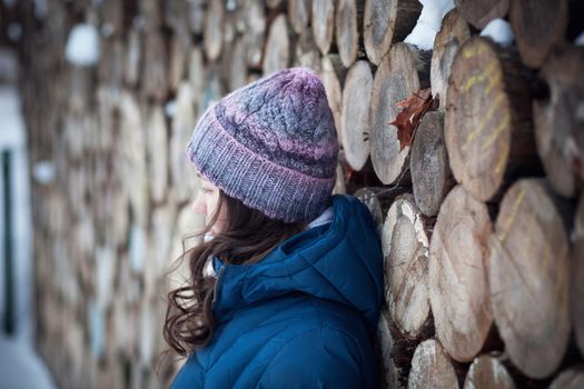 the beautiful young girl in a warm cap from wool of the alpaca in the winter forest. knitting