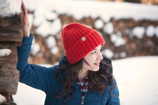 the beautiful young girl in a warm cap from wool of the alpaca in the winter forest. knitting