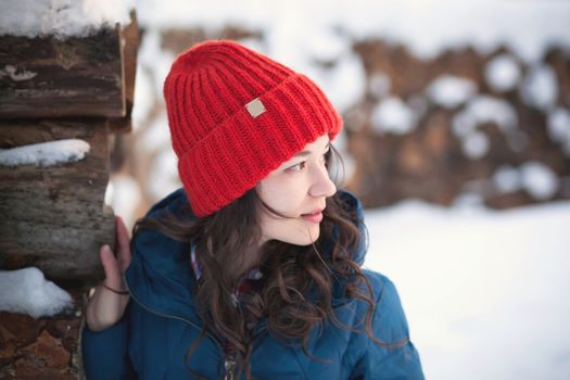 the beautiful young girl in a warm cap from wool of the alpaca in the winter forest. knitting