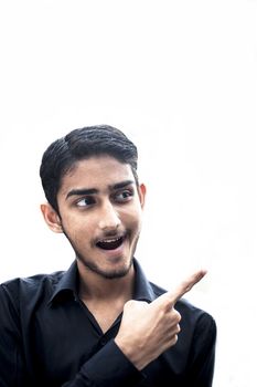 Close up of young Caucasian man with bear isolated opens mouth widely and stares at the camera while pointing towards the blank side.