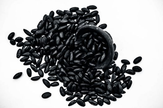 Close up of brown colored dried custard apples or sitaphal or sugar apple seeds in a black colored clay bowl isolated on white.