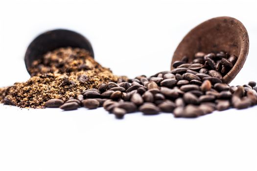 Close up of brown colored dried custard apples or sitaphal or sugar apple seeds in a black colored clay bowl and its powder of grounded seeds in a brown colored clay bowl isolated on white.