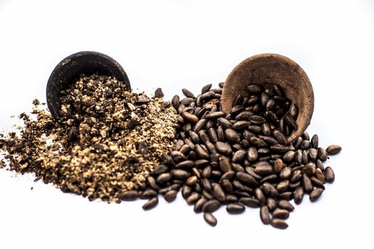 Close up of brown colored dried custard apples or sitaphal or sugar apple seeds in a black colored clay bowl and its powder of grounded seeds in a brown colored clay bowl isolated on white.