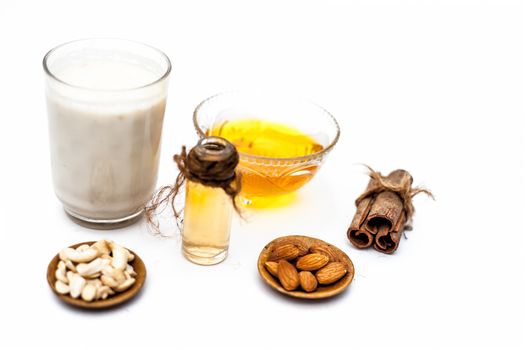 Close up of popular Indian &amp; Asian winter drink isolated on white i.e Honey milk or shahad ka dudh in a transparent glass with entire ingredients which are milk,honey, and dry fruits.