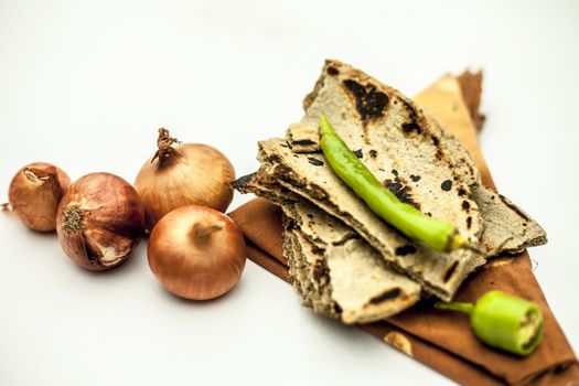 Poor man's lunch or farmer's lunch isolated on white or common items eaten in lunch isolated on white which are bajri ki roti with cut and raw onion along with green chili.