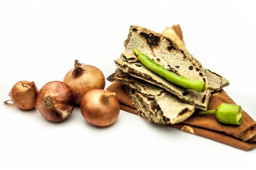 Poor man's lunch or farmer's lunch isolated on white or common items eaten in lunch isolated on white which are bajri ki roti with cut and raw onion along with green chili.