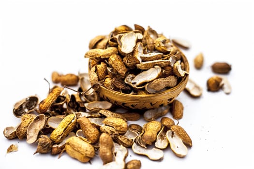 Close up of brown colored hamper having groundnuts or peanuts or moongaphalee or Arachis hypogaea or goober or monkey nut some in shells and some opened isolated on white.