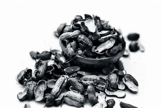 Close up of brown colored hamper having groundnuts or peanuts or moongaphalee or Arachis hypogaea or goober or monkey nut some in shells and some opened isolated on white.