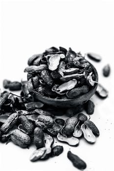 Close up of brown colored hamper having groundnuts or peanuts or moongaphalee or Arachis hypogaea or goober or monkey nut some in shells and some opened isolated on white.