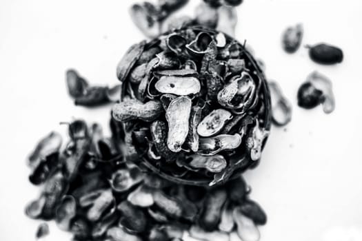 Close up of brown colored hamper having groundnuts or peanuts or moongaphalee or Arachis hypogaea or goober or monkey nut some in shells and some opened isolated on white.