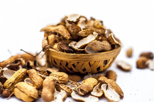 Close up of brown colored hamper having groundnuts or peanuts or moongaphalee or Arachis hypogaea or goober or monkey nut some in shells and some opened isolated on white.