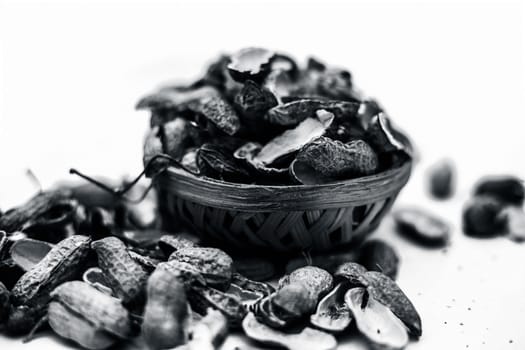 Close up of brown colored hamper having groundnuts or peanuts or moongaphalee or Arachis hypogaea or goober or monkey nut some in shells and some opened isolated on white.