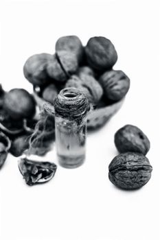 Close up of essential oil or essence of walnut or akhrot isolated on white in a small transparent glass bottle along with raw in shell walnuts or Juglans.