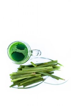 Close up of fresh organic extracted juice of lemon grass isolated on white in a transparent glass with raw Indian lemon grass or lili chai or Cymbopogon.