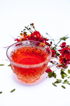 Close up of orange colored herbal floral tea of peacock flower or Caesalpinia pulcherrima in a transparent cup along with raw flower isolated on white.