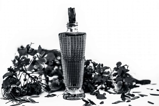 Close up shot of perfume or scent of peacock flower in a transparent bottle along with raw flowers isolated on white.