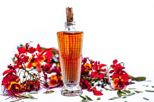 Close up shot of perfume or scent of peacock flower in a transparent bottle along with raw flowers isolated on white.