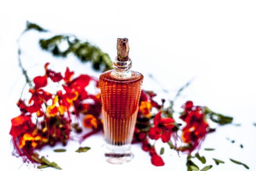 Close up shot of perfume or scent of peacock flower in a transparent bottle along with raw flowers isolated on white.