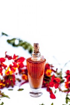 Close up shot of perfume or scent of peacock flower in a transparent bottle along with raw flowers isolated on white.