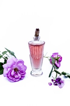 Close up shot of perfume or scent or spray of rose or rosa or gulab in a transparent glass bottle isolated on white along with rose flowers.