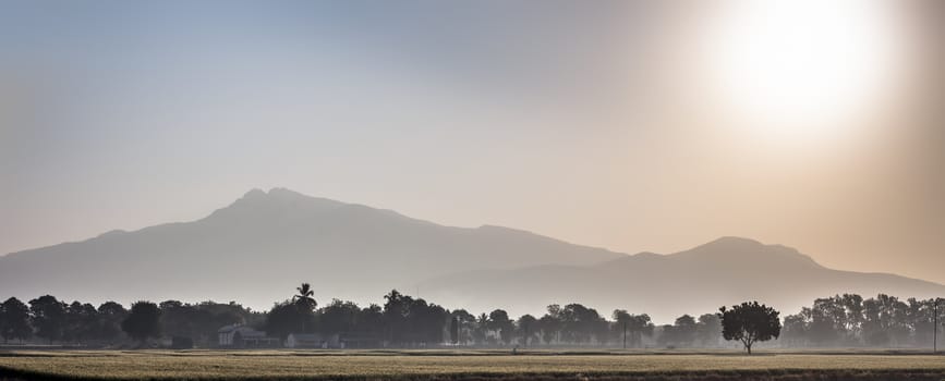 Wide landscape shot of sunrise through mountains in the early morning through fields with mist and fog.