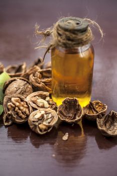 Close up of herbal organic extracted walnut oil in a transparent glass bottle with raw wall nuts on wooden surface.