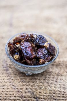 Close up of shot of raw organic dates or khajoor or Phoenix dactylifera in a glass bowl on a gunny bag background.