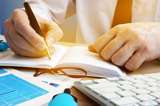 Businessman writing in a notepad. Workplace in the office.