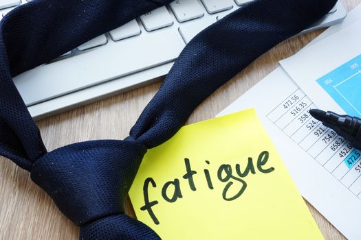 Tie and memo stick with word fatigue on an office desk.