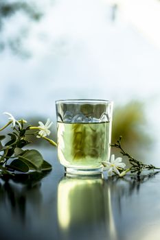 Close up of extract of Indian jasmine flower or juhi or Jasminum Auriculatum on wooden surface in a transparent glass with raw flowers.