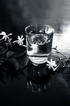 Close up of extract of Indian jasmine flower or juhi or Jasminum Auriculatum on wooden surface in a transparent glass with raw flowers.