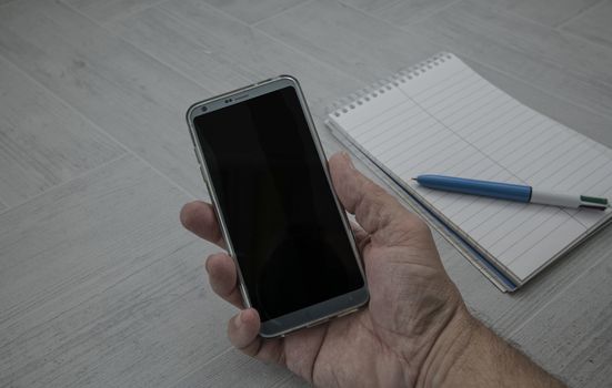 male hand holding mobile phone with paperwork and pen as background