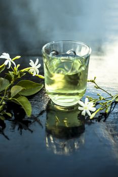 Close up of extract of Indian jasmine flower or juhi or Jasminum Auriculatum on wooden surface in a transparent glass with raw flowers.